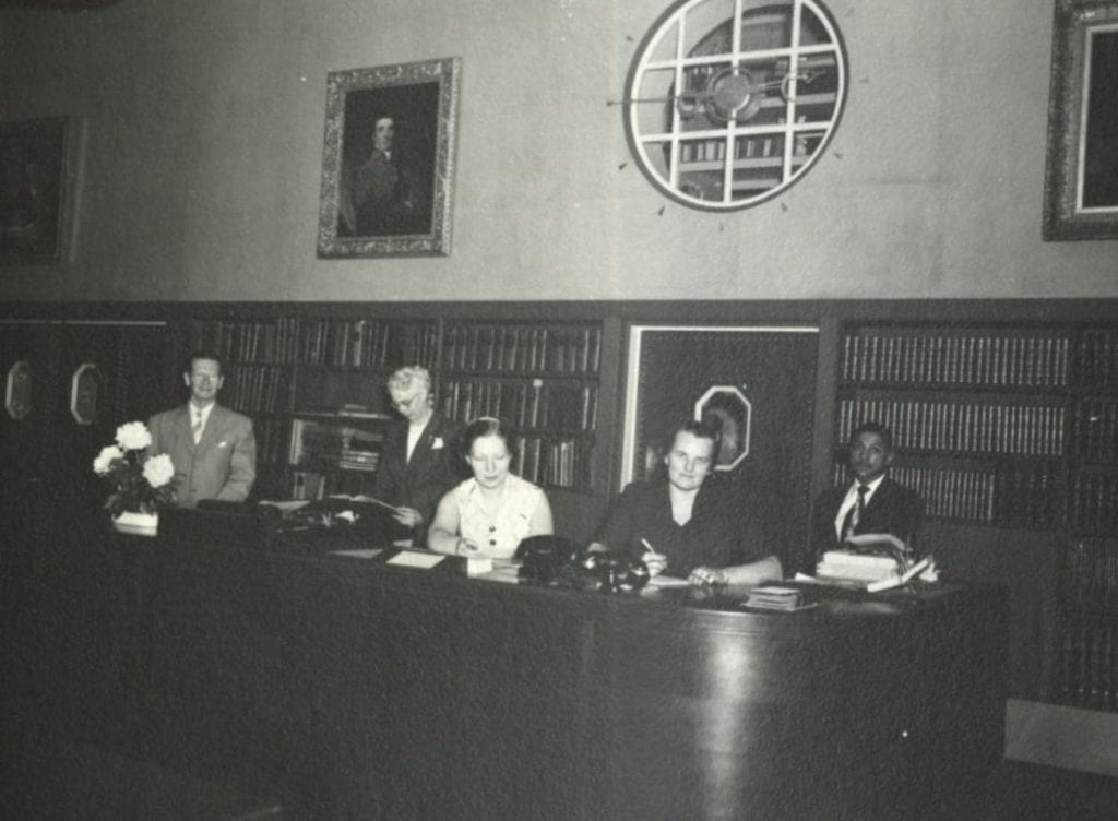 Five people stand behind a library reading room service desk.